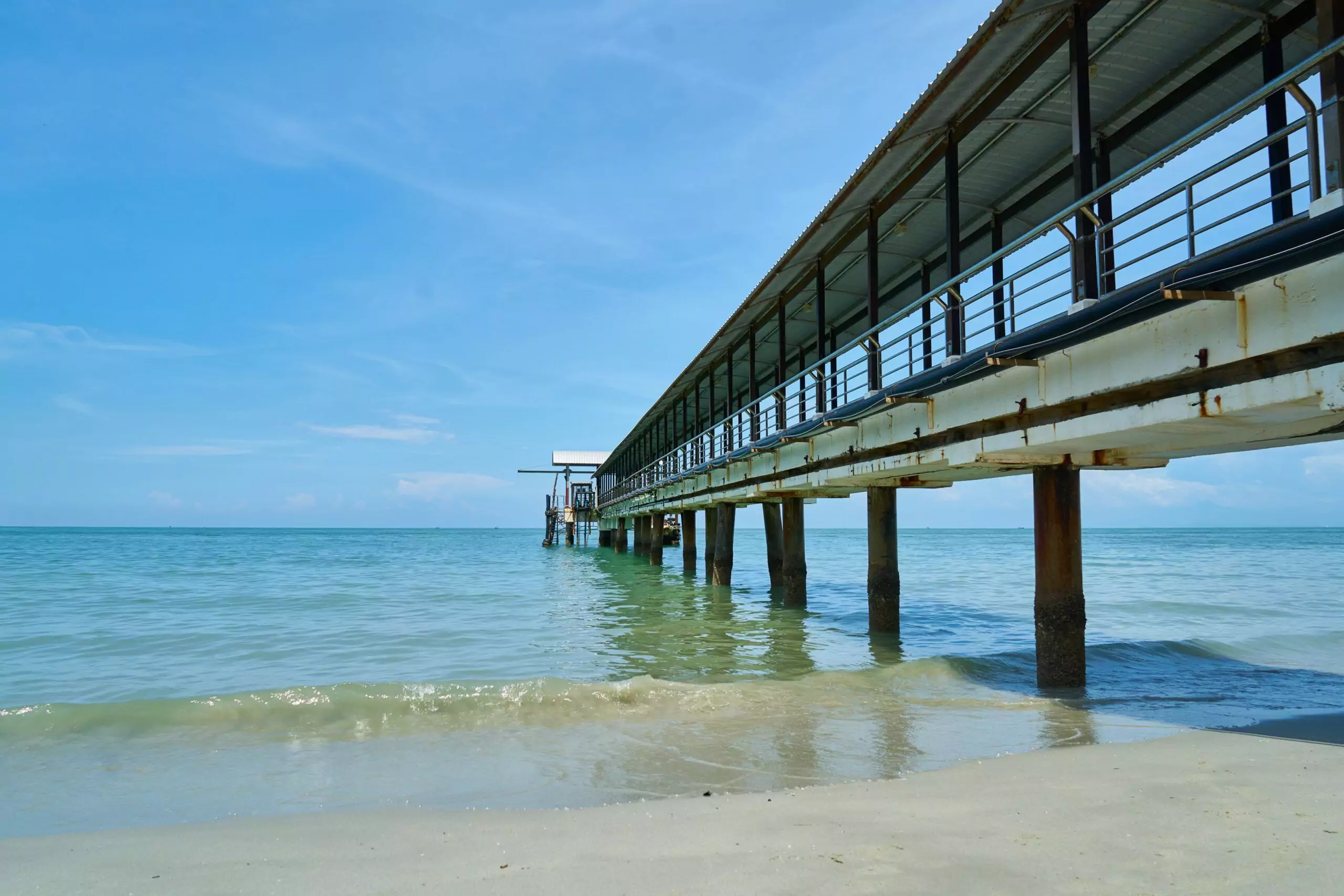 Ocean water and a pier viewed from a sandy beach